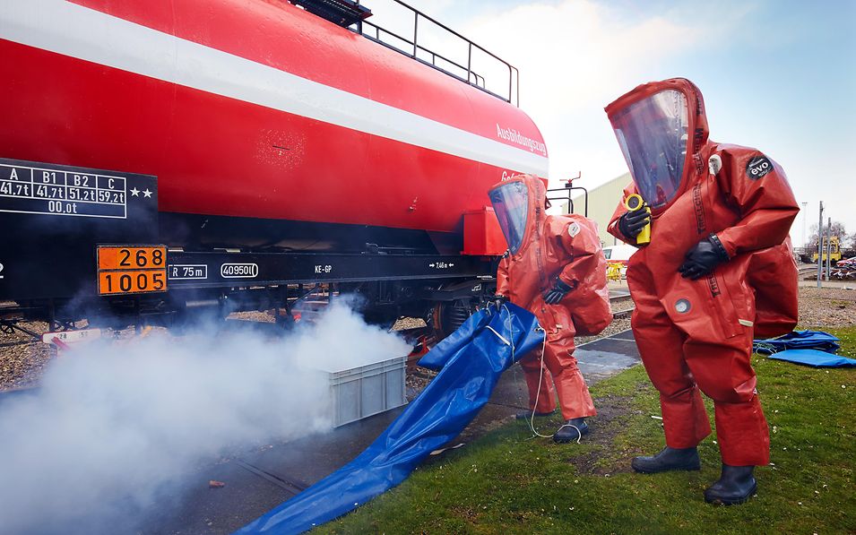 People wearing red protective suits next to a tank wagon.