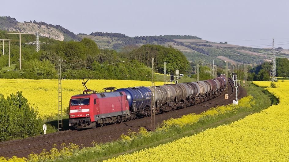 Zug mit Kesselwagen fährt durch Rapsfelder