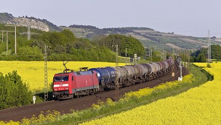 Train with tank wagon runs through rapeseed fields