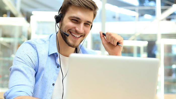 Junger Mann mit Headset vor Laptop.