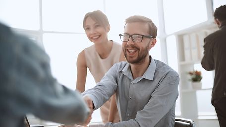 Drei Mitarbeiter:innen begrüßen neue Person mit Handshake.
