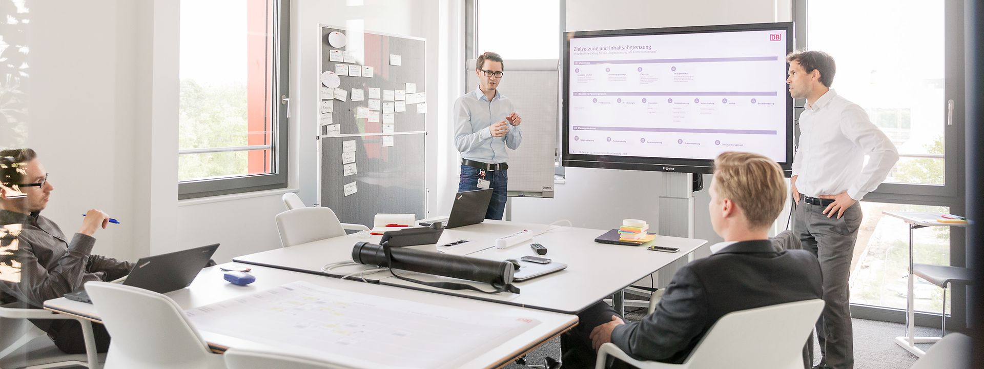 Vier Mitarbeiter in Diskussion vor Smartboard