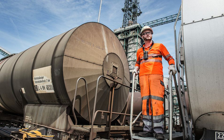 Foreman shunter in safety clothing stands on the ladder of a tank wagon.