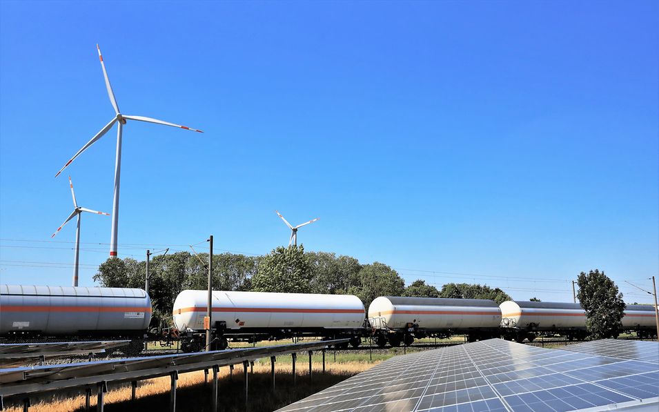 Green landscape with wind turbines, solar panels and a passing train