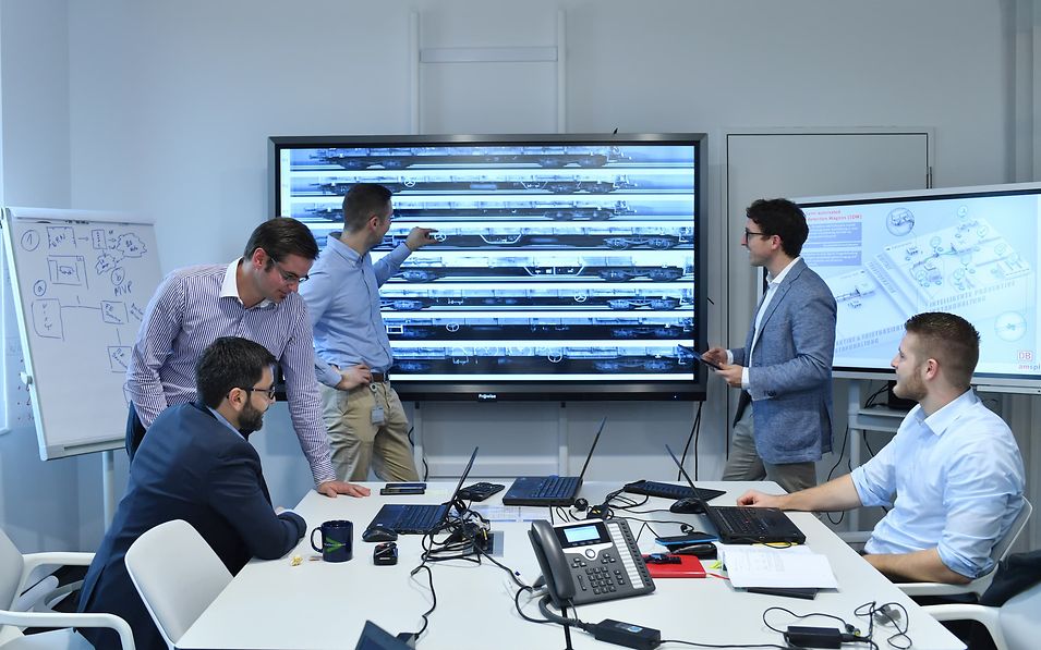Five employees in front of a smartboard.