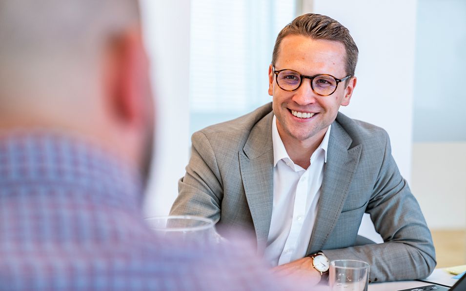 Smiling man in a suit in conversation with another man.