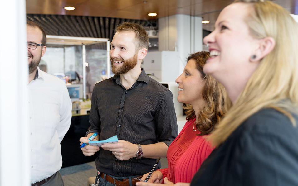 Four cheerful employees in front of a pinboard.